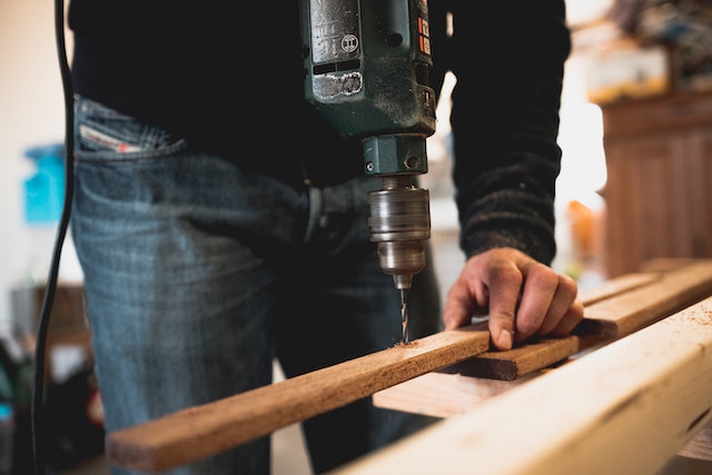 person using electric drill to make a small hole in a thin piece of wood